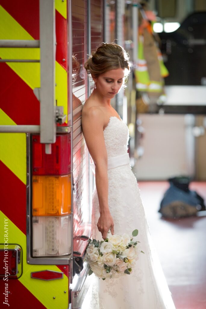 A bride in white holding flowers standing next to an ambulance.
