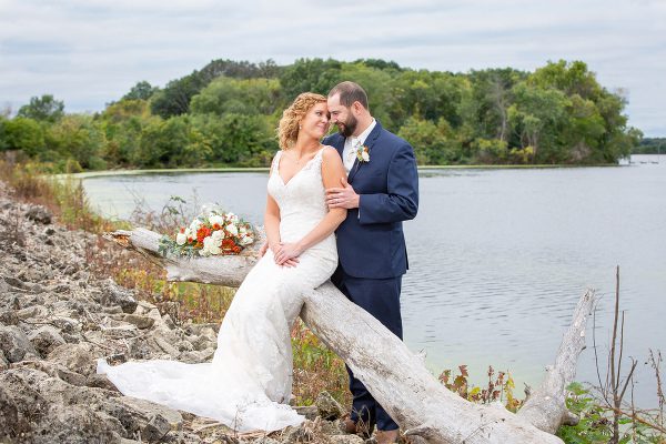 A bride and groom pose for a picture on the shore of a lake.