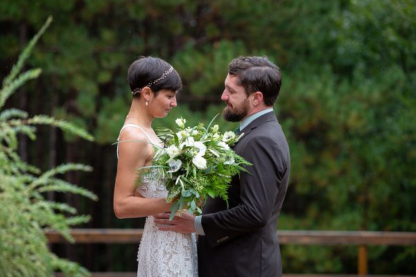 A man and woman holding flowers in front of trees.