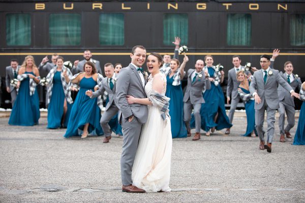 A bride and groom pose for a picture in front of a train.