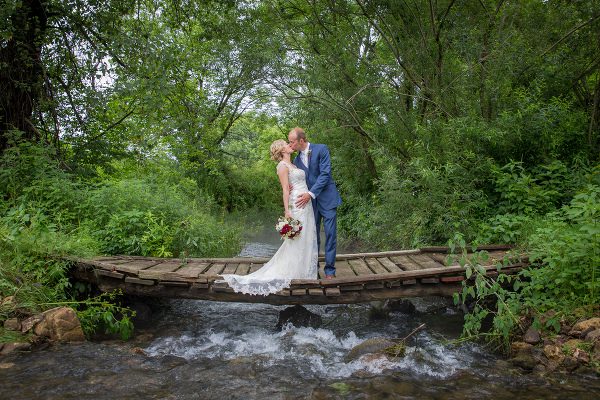 A bride and groom kissing on the bridge over water.