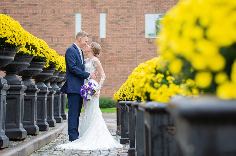 A bride and groom kissing in front of yellow flowers.