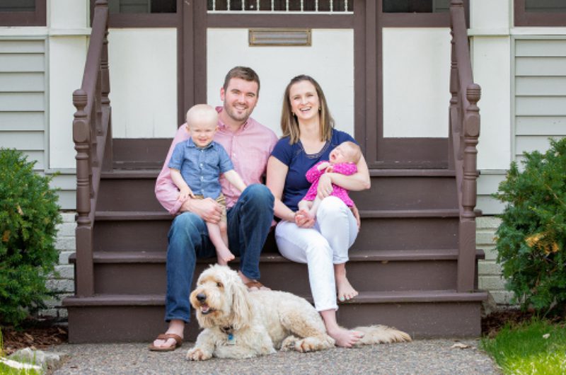 A family sitting on the steps with their dog.