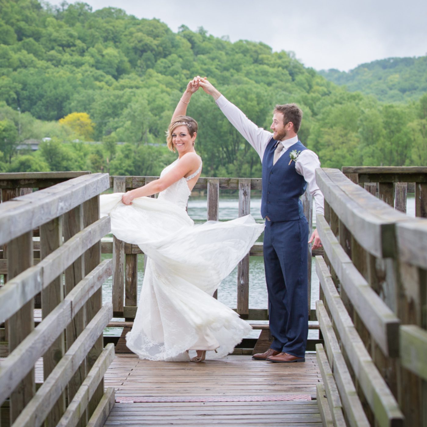 A bride and groom pose for the camera on a bridge.
