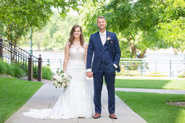 A bride and groom pose for a picture on the sidewalk.
