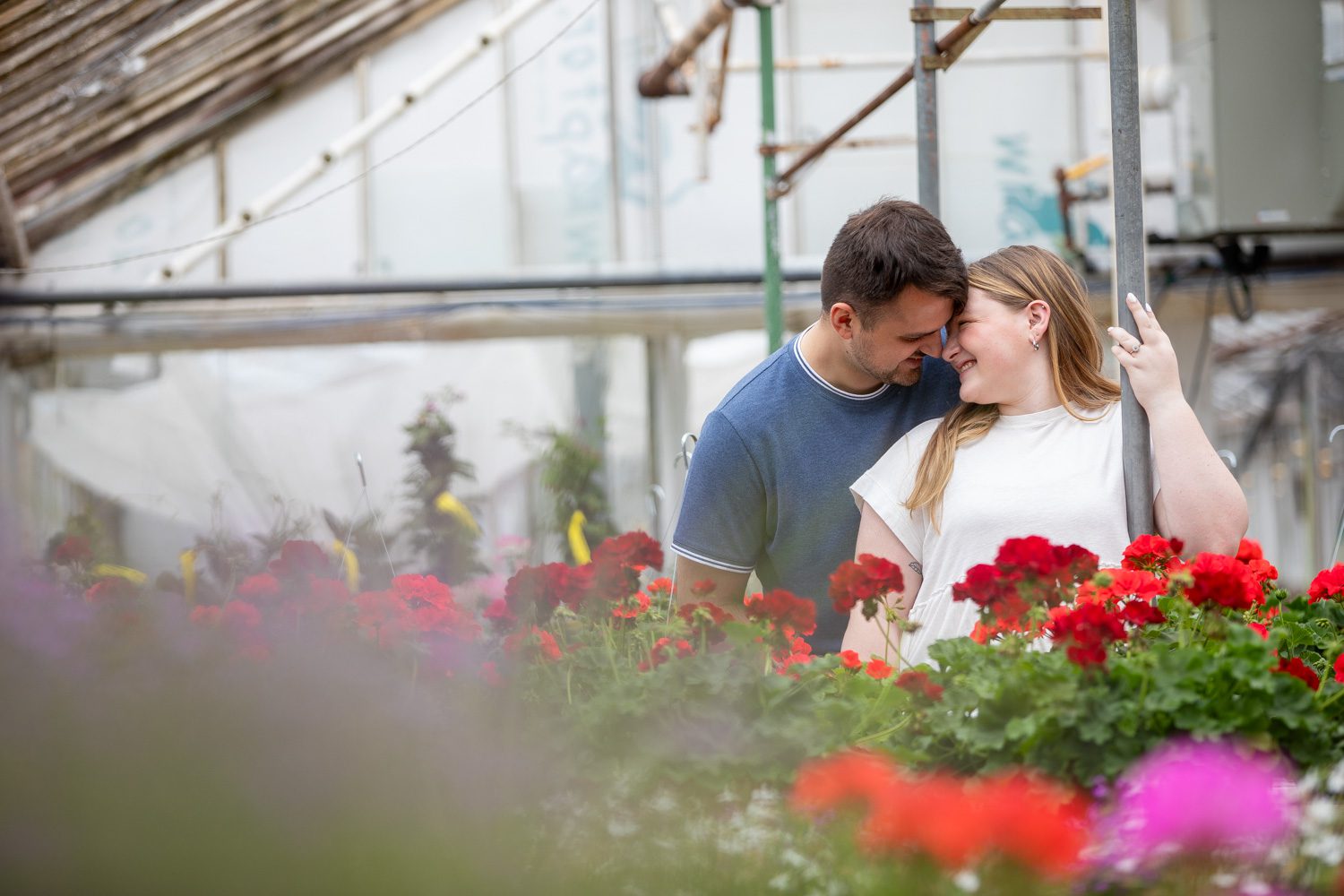 Pretty red flowers in the foreground of an intimate moment during a greenhouse engagement session.