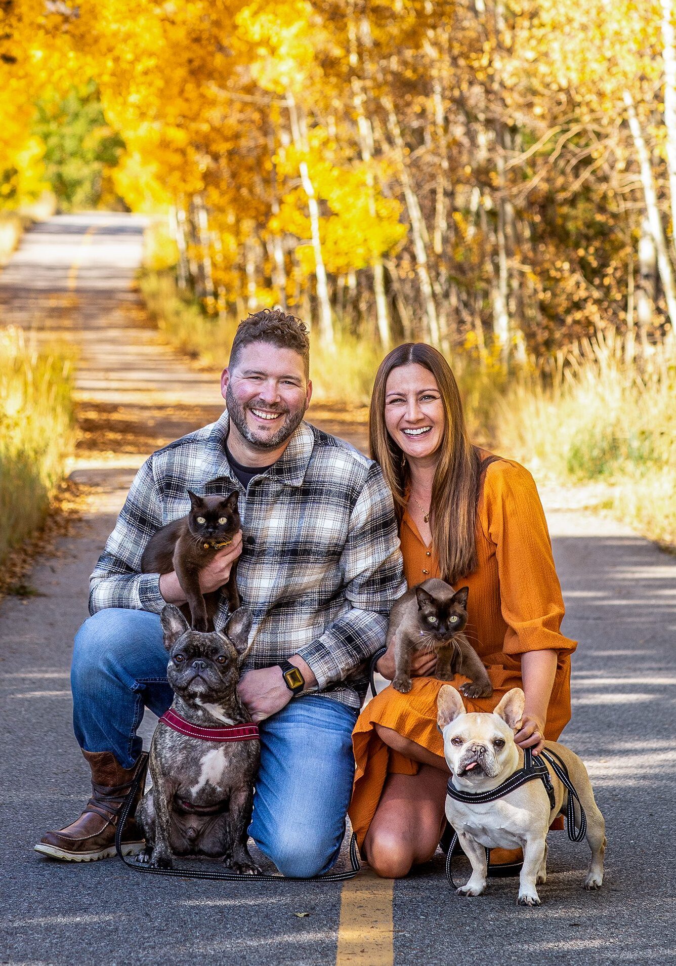 Smiling couple with pets on golden autumn road